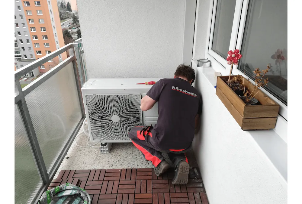 Technik Klimahome montuje venkovní jednotku klimatizace na balkoně bytového domu